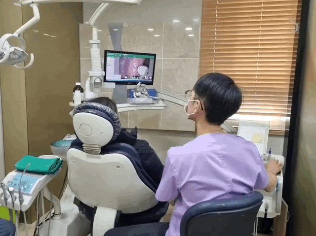 치과 진료실에서 환자가 치과 의자에 앉아 있고, 치과의사가 모니터를 보며 진료를 설명하는 모습